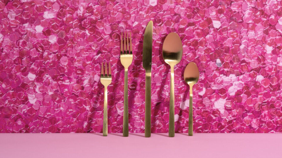 Goldfarbenes Besteck-Set vor pinkfarbenem Glitzer-Hintergrund