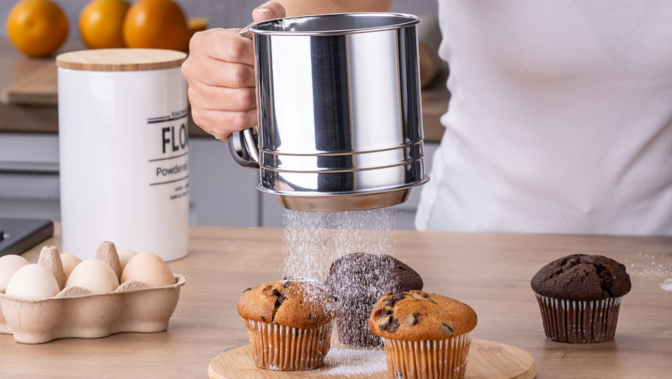 Muffins auf einem Servierbrett, die mit Puderzucker bestäubt werden Muffins auf einem Servierbrett, die mit Puderzucker bestäubt werden