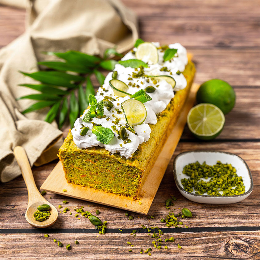 Angeschnittener veganer Carrot Cake auf einem Holzbrett, daneben Pistazien in einer Schale