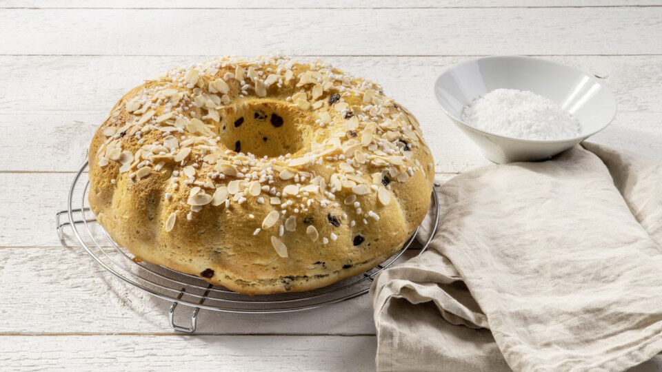 Hefekranz auf einem runden Kuchengitter, daneben ein Geschirrtuch und eine Schüssel