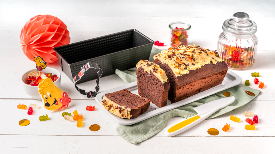 Schokoladen-Kastenkuchen mit Topping auf einer Servierplatte, daneben eine Kastenform und Dekoration Schokoladen-Kastenkuchen mit Topping auf einer Servierplatte, daneben eine Kastenform und Dekoration