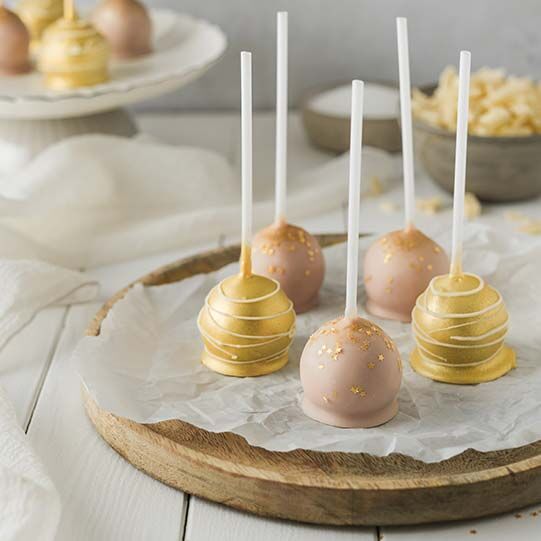 Cake Pops in rosa und gold auf einer Tortenplatte aus Holz