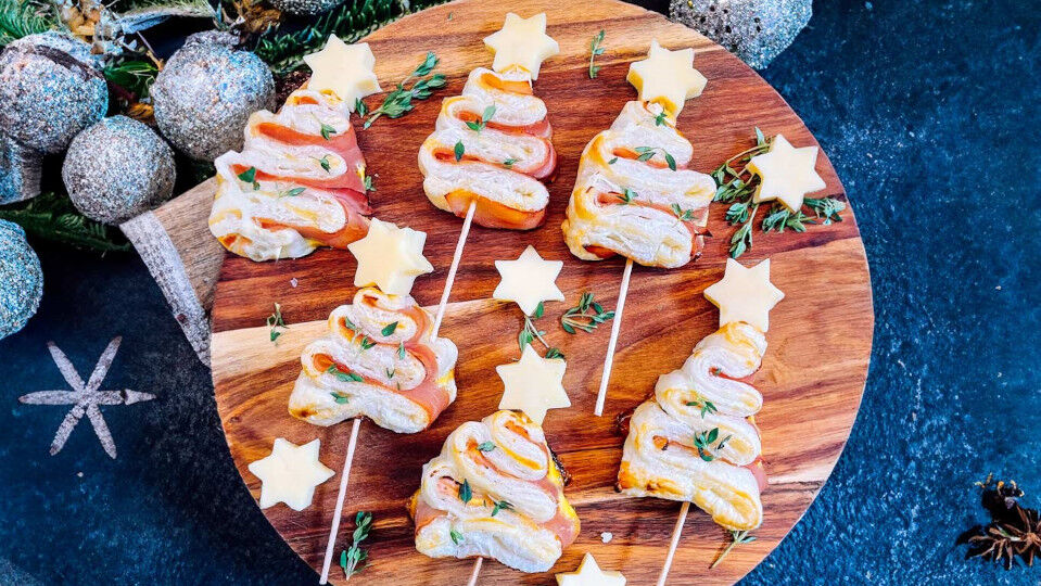 Herzhafte Blätterteig-Tannenbäume mit Käse und Schinken auf einem runden Servierbrett aus Holz