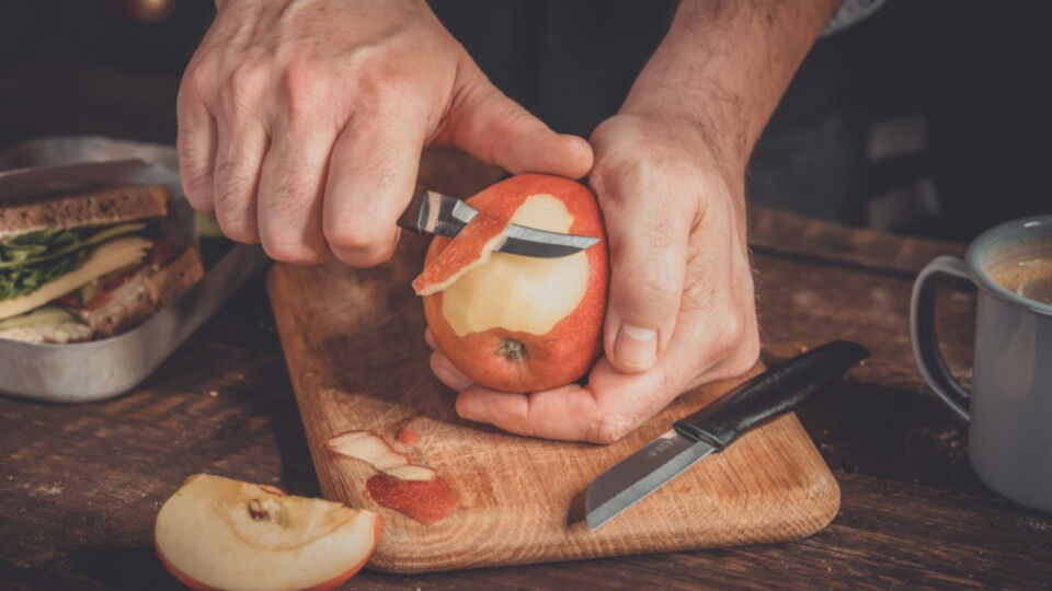 Ein ganzer Apfel mit roter Schale, der gerade auf einem Schneidebrett geschält wird