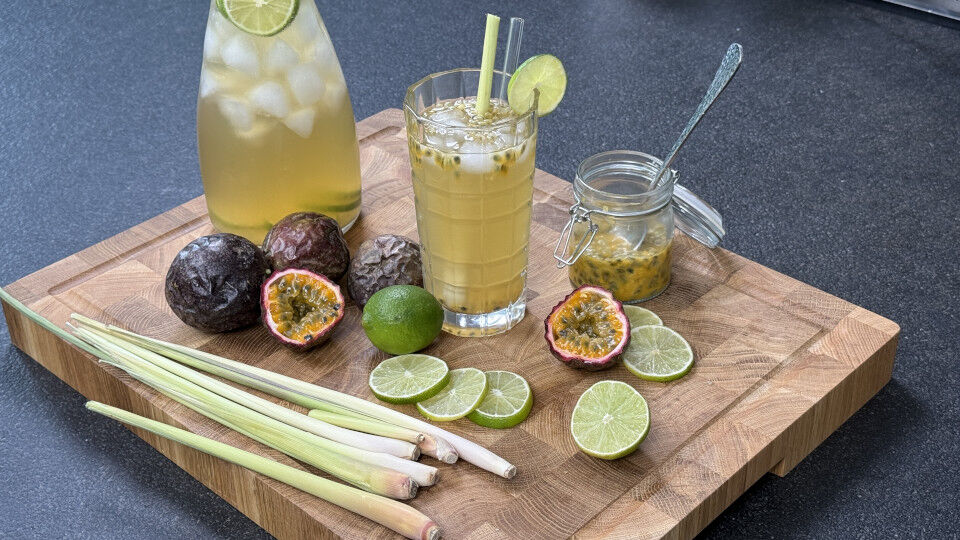 Maracuja-Eistee im Glas mit aufgeschnittenen Maracujas und Limetten daneben